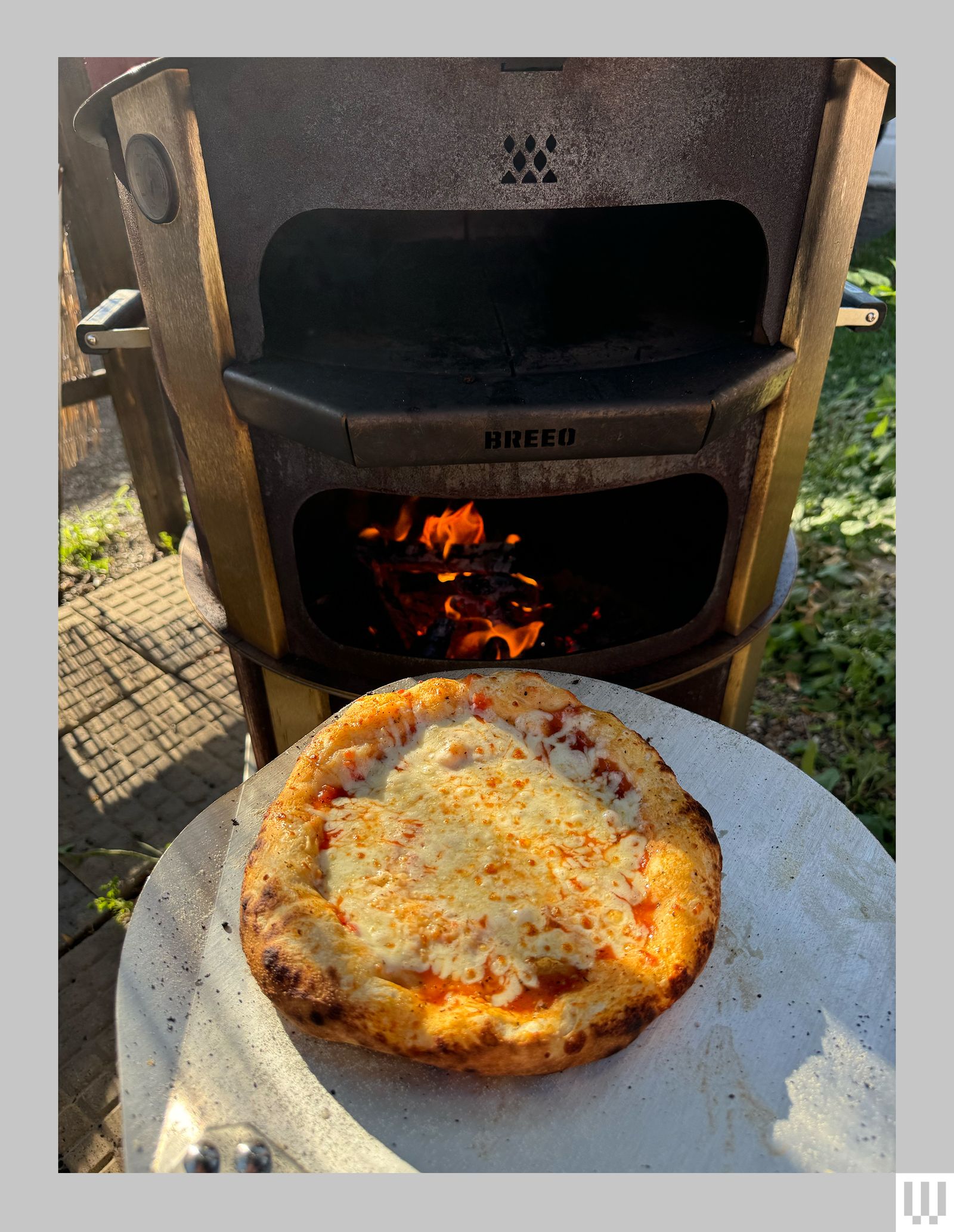 Pizza oven with a fire stoked inside and a pizza presented beside it