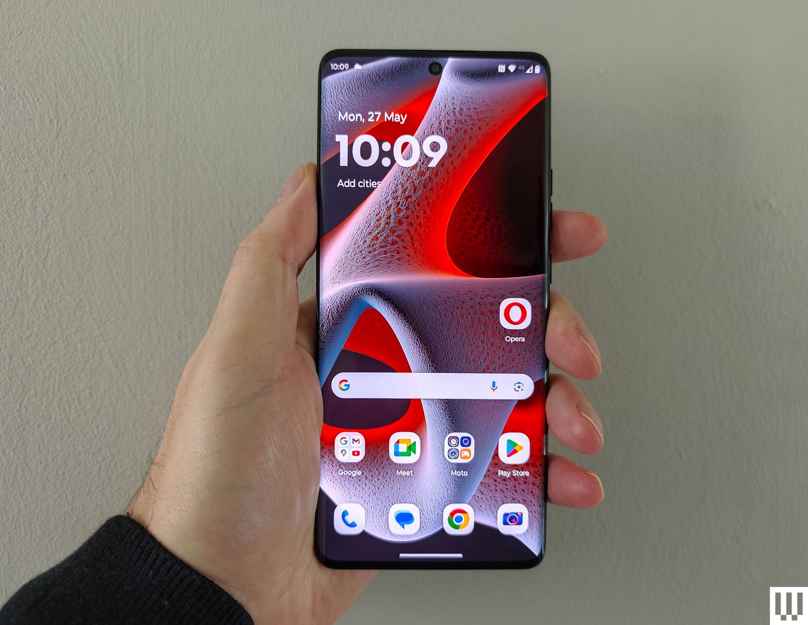 Hand holding a slim mobile phone with rounded edges and the screen displaying an abstract wallpaper and app icons